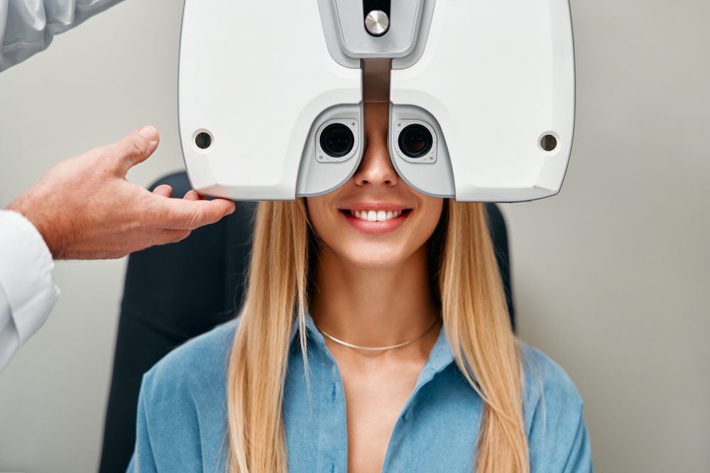 A woman is smiling while undergoing an eye exam with a phoropter at an optometry clinic - Carrboro Eye Doctor A woman is smiling while undergoing an eye exam with a phoropter at an optometry clinic - Carrboro Eye Doctor