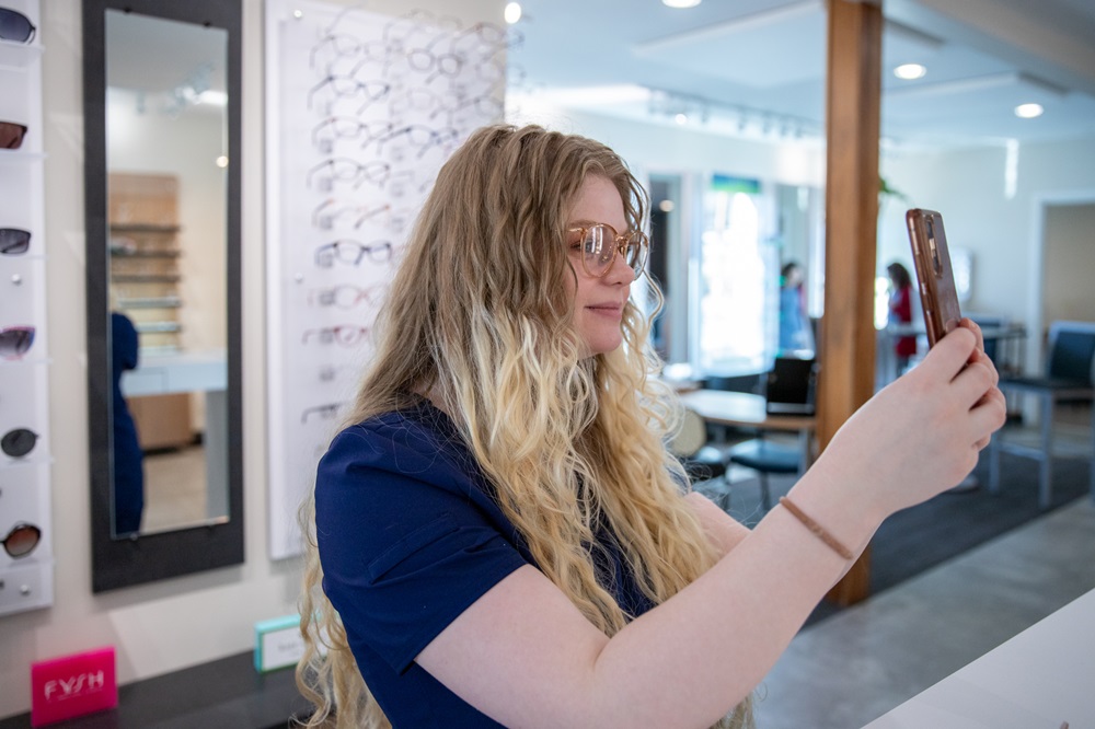 A woman in an optical shop takes a selfie while trying on a pair of glasses - Carrboro Eye Doctor A woman in an optical shop takes a selfie while trying on a pair of glasses - Carrboro Eye Doctor