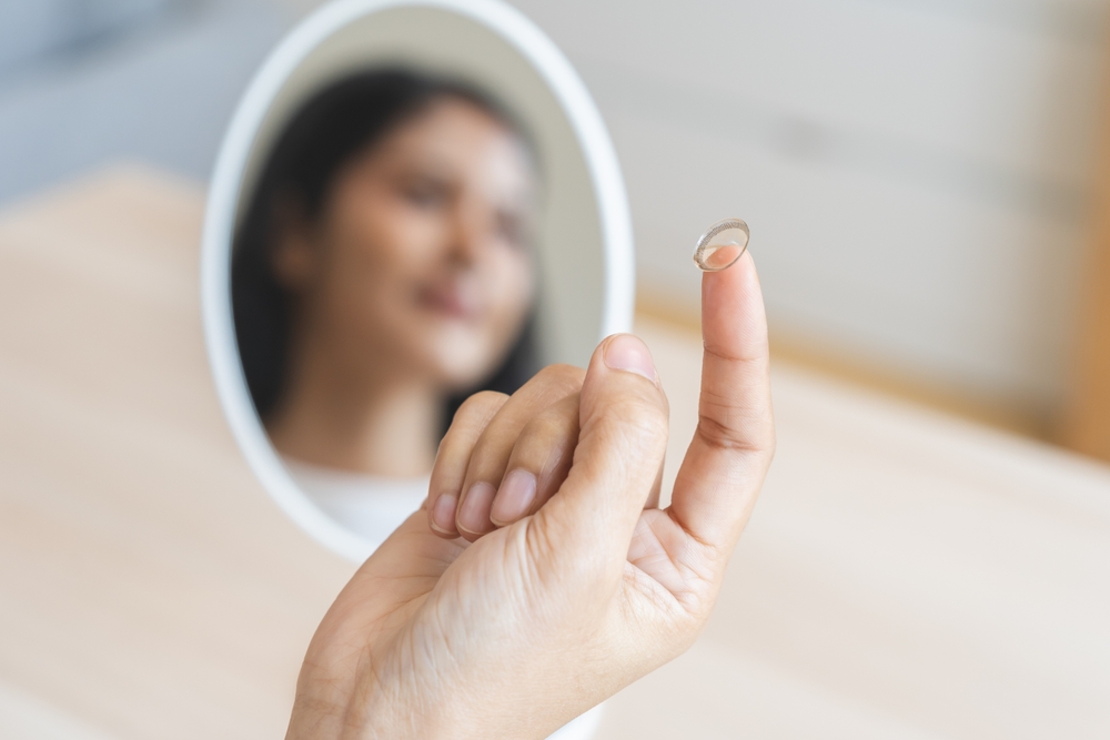A person holding a contact lens on their fingertip with a mirror in the background - Carrboro Eye Doctor A person holding a contact lens on their fingertip with a mirror in the background - Carrboro Eye Doctor